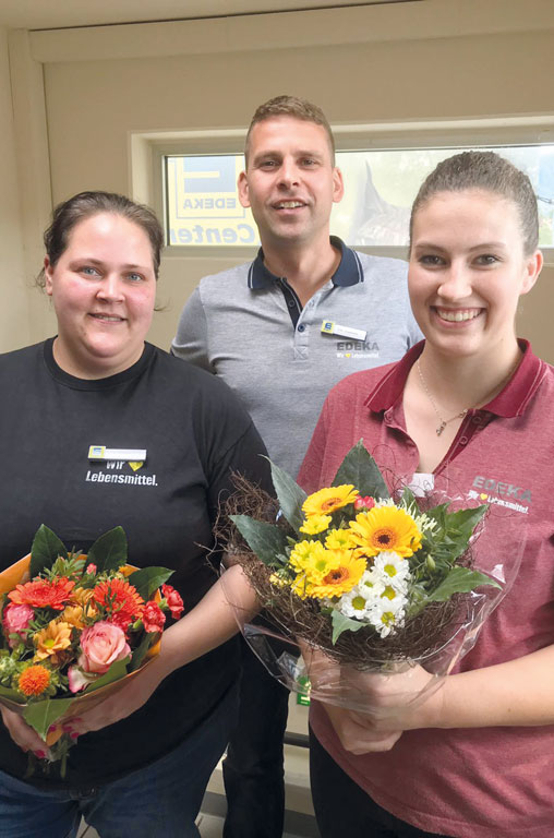 Kaufmann Ronny Lunze gratuliert zwei Auszubildenden mit Blumensträußen zur bestandenen Prüfung.