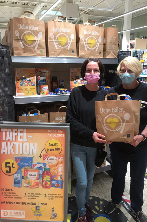 Zwei Mitarbeiterinnen zeigen die Spendentüten im Wert von 5 Euro mit bunten Lebensmitteln